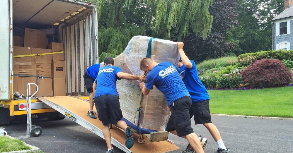 Movers are pushing a heavy package onto their moving truck
